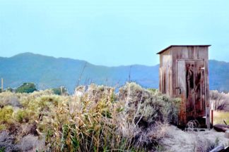 photo: weathered outhouse in the empty desert, mountainous backdrop. Title: Room With a View
