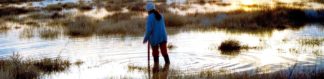 Photo: woman silhouetted against sunset reflected in the flooded field where she is wading (Mojave Desert)